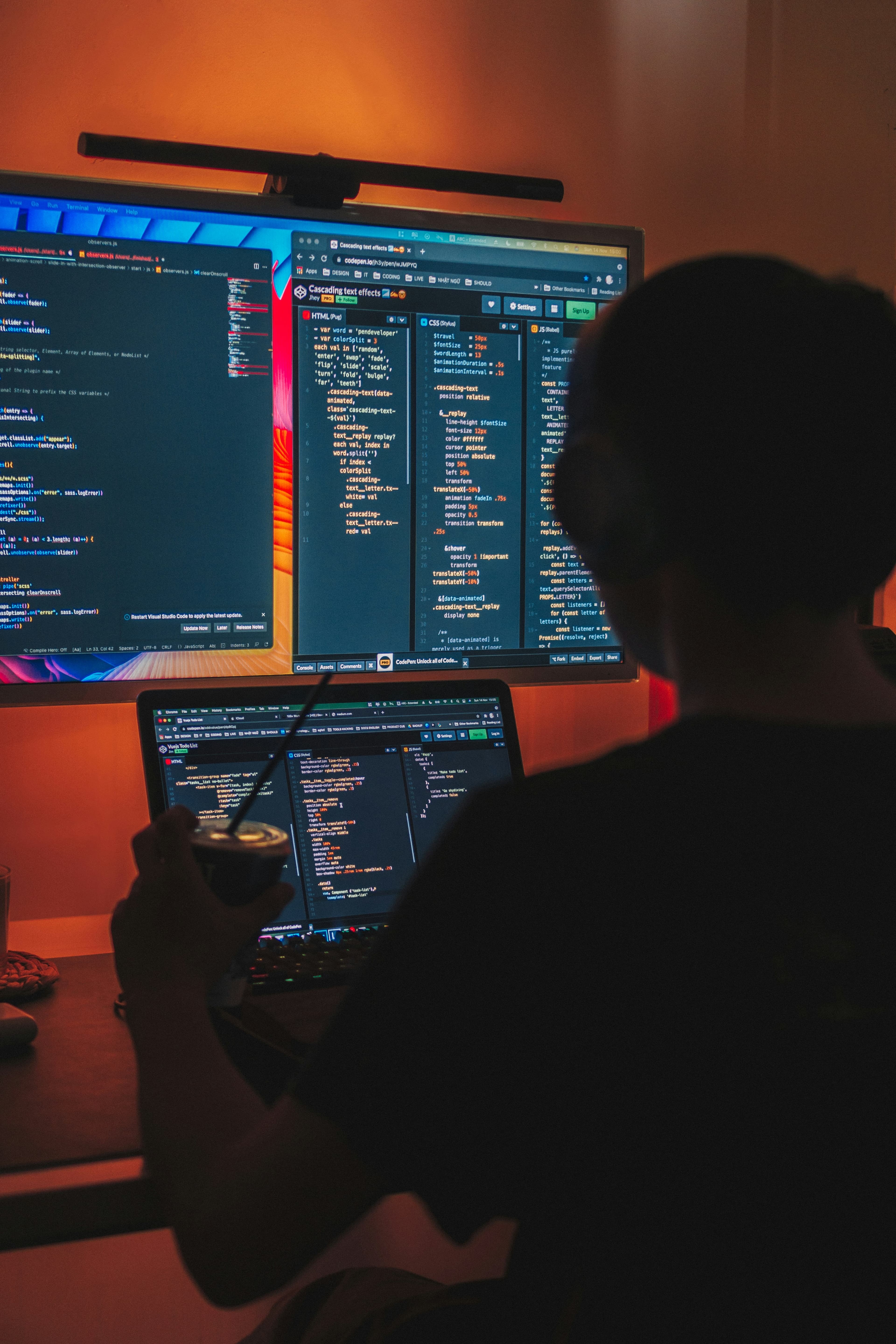 A developer writing code at a dual-monitor setup in warm evening light